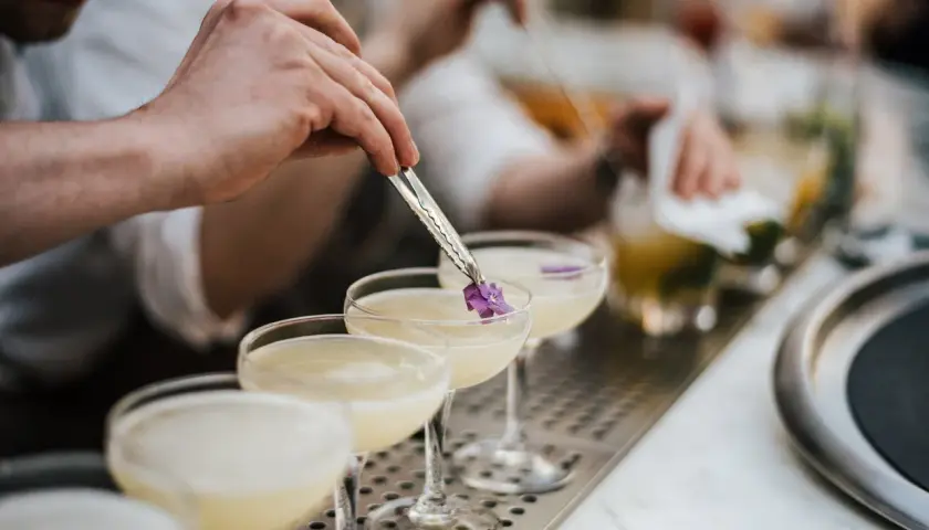 Ein Barkeeper garniert einen Cocktail mit Cointreau und Sekt mit einer kleinen Blüte.
