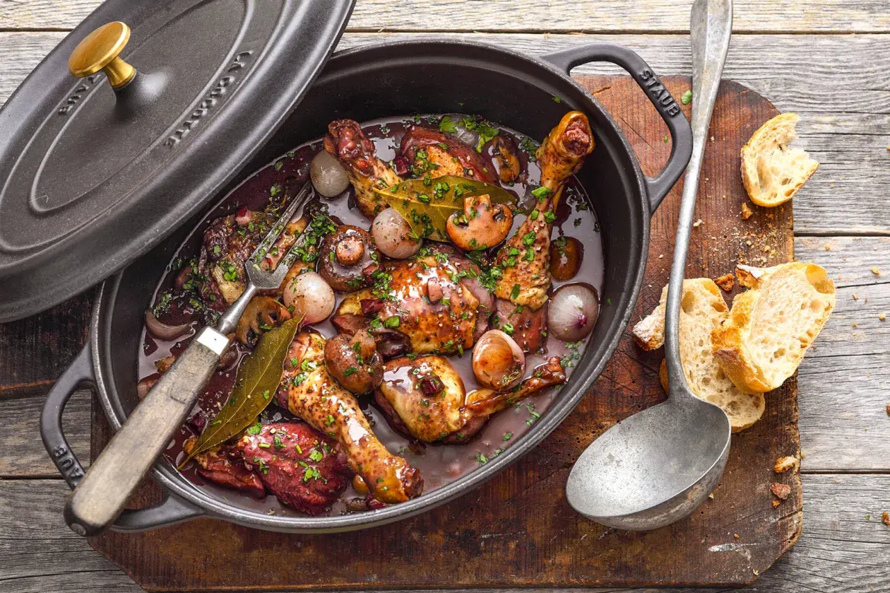 Ein köstliches Coq au Vin ganzes Huhn in dunkler Sauce mit Pilzen und Zwiebeln, serviert in einem Gusseisentopf. Dazu Baguette.