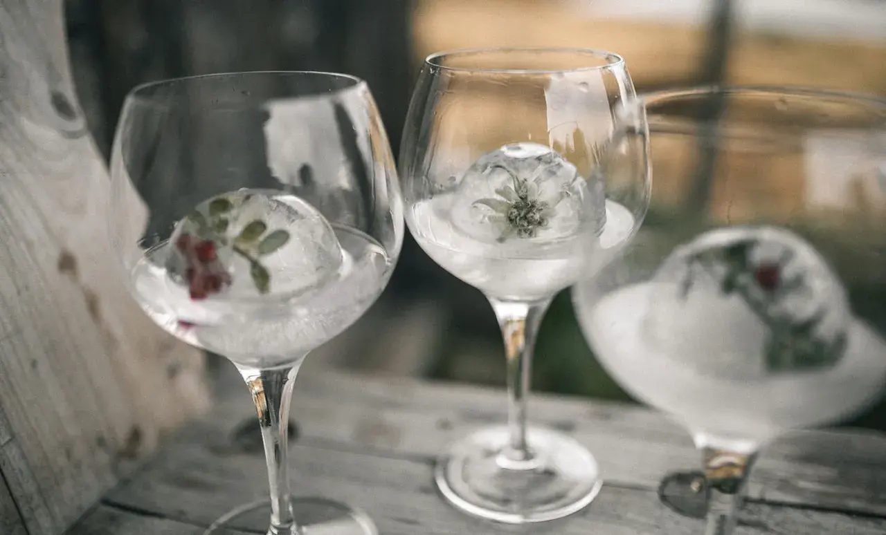 Drei Gläser mit Gin Tonic, gekühlt mit Eisbällen, die Kräuter und Beeren enthalten.