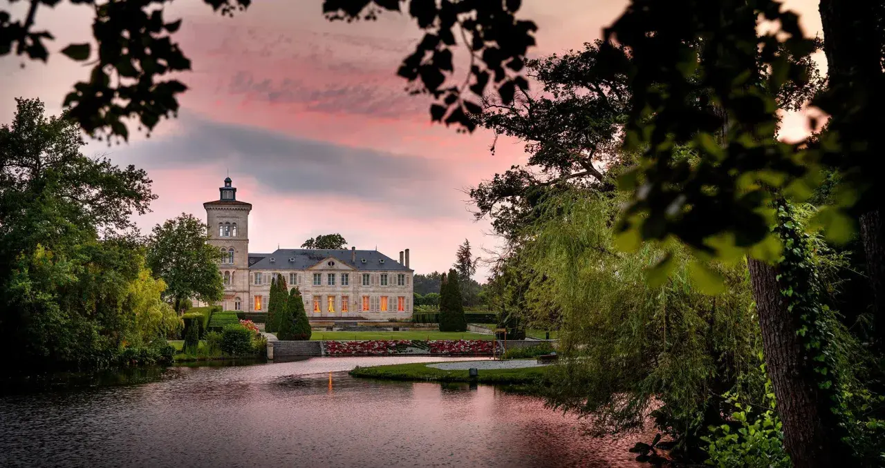 Schloss Saint Julien am See, umgeben von Bäumen, bei Sonnenuntergang mit rosa Himmel.