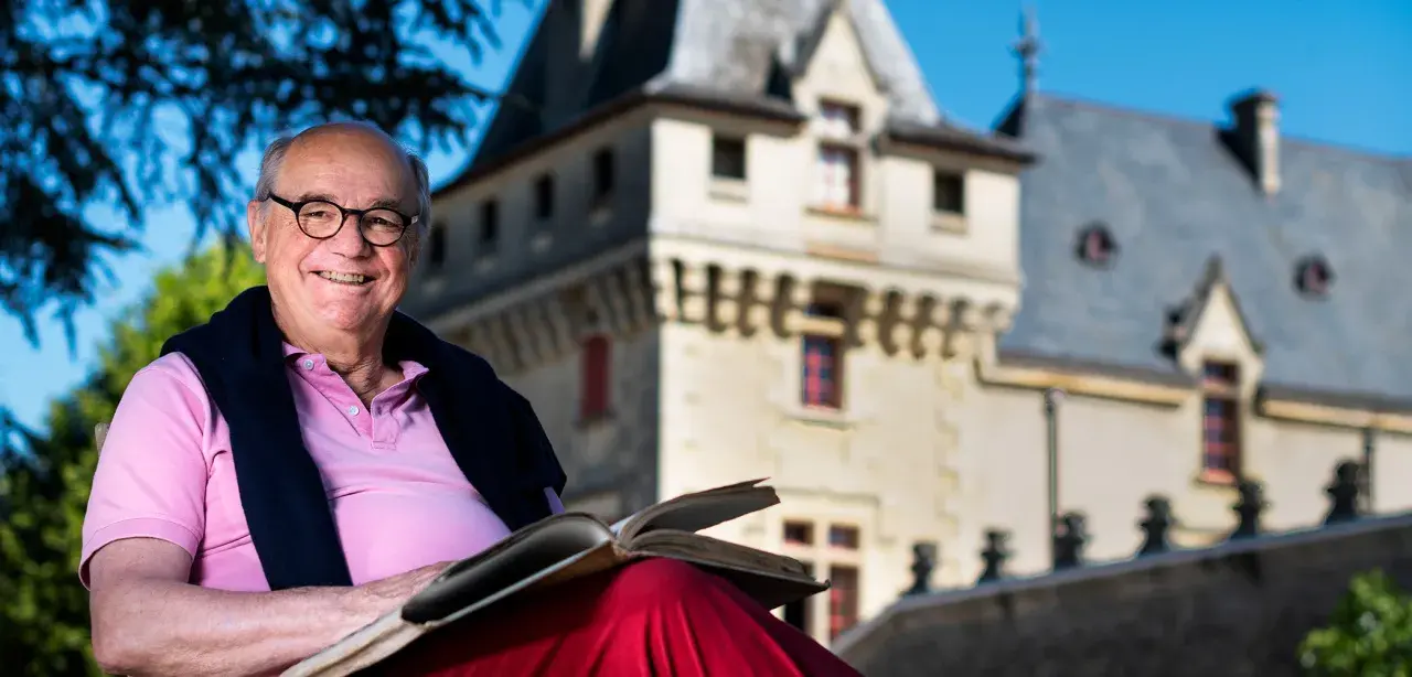 Ein Mann mit Brille liest ein Buch vor dem **Château de Pressac**.