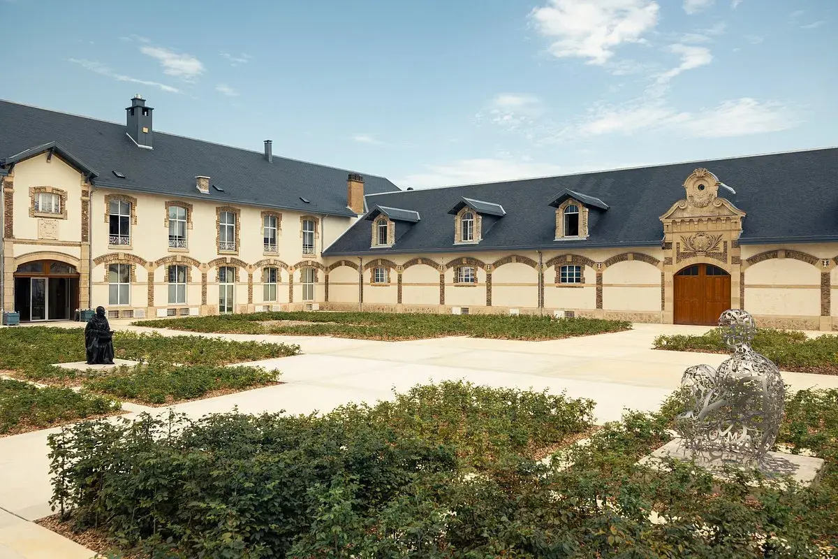 Der Innenhof von Maison Ruinart mit moderner Skulptur und grünen Büschen.