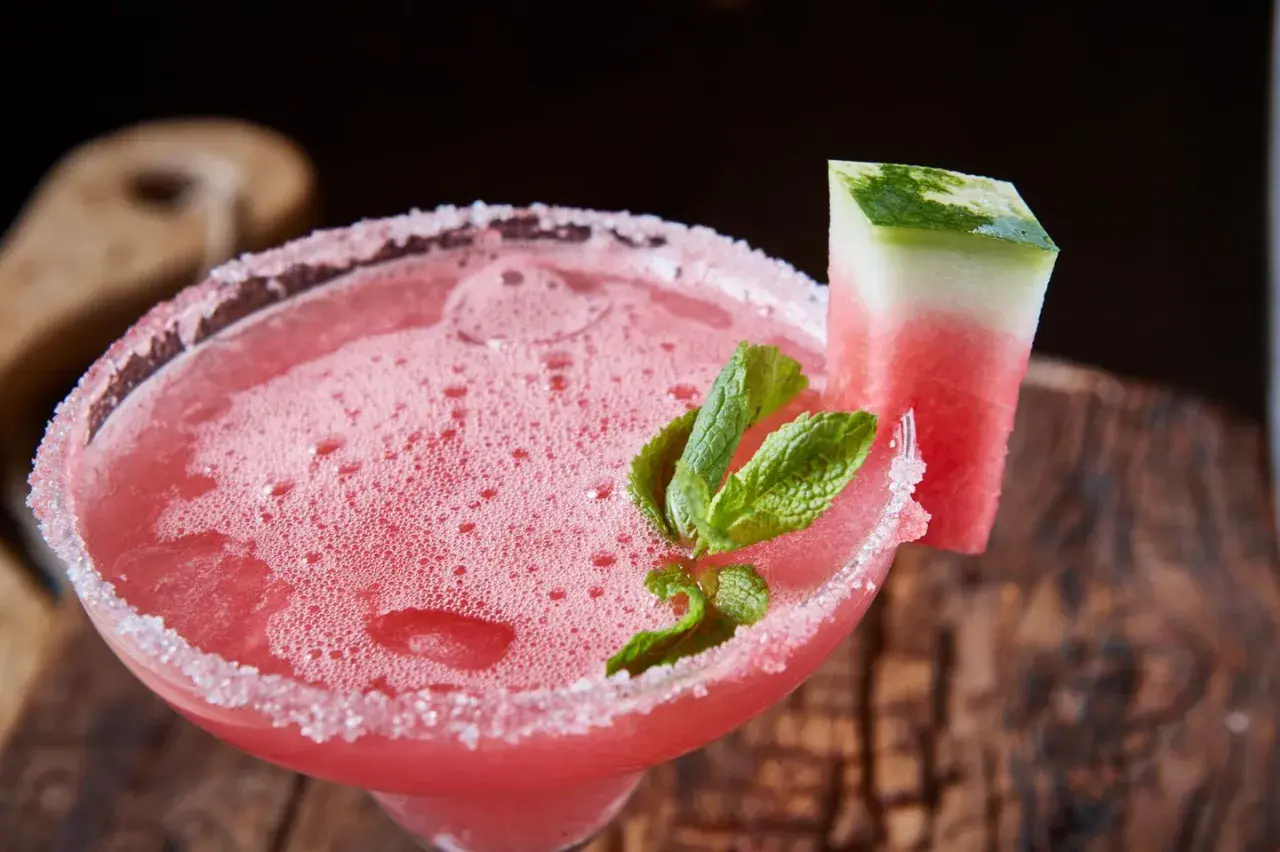 Erfrischender weihnachtscocktail mit sekt, garniert mit Wassermelone und Minze, auf rustikalem Holz.