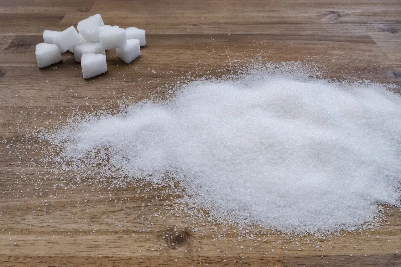 Zuckerwürfel und ein Haufen feiner Zuckerkristalle auf Holz. Ein visueller Hinweis auf den trauben zuckergehalt in Lebensmitteln.