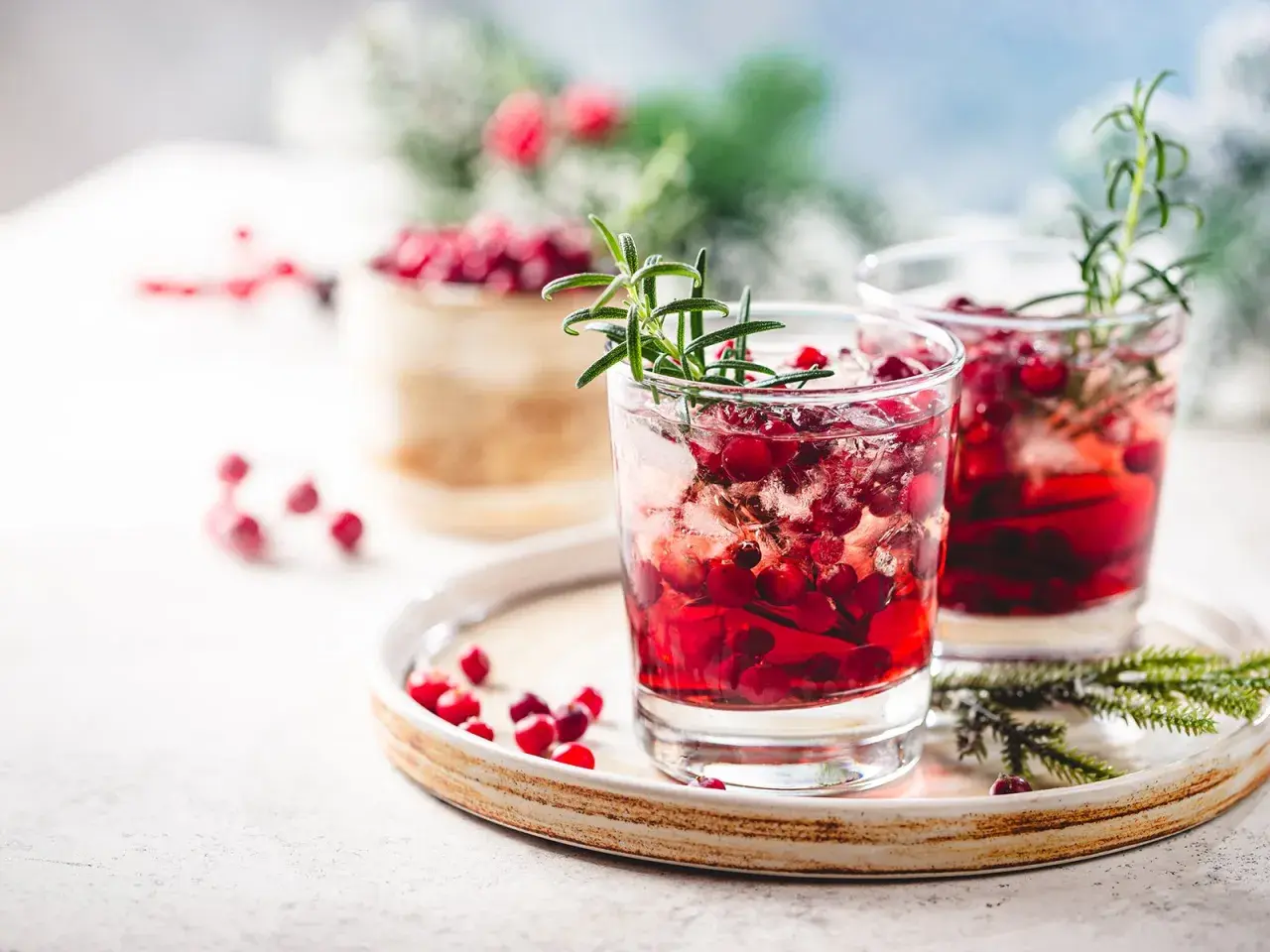Zwei erfrischende Silvester Cocktails mit Gin, Cranberries und Rosmarin auf einem Teller.