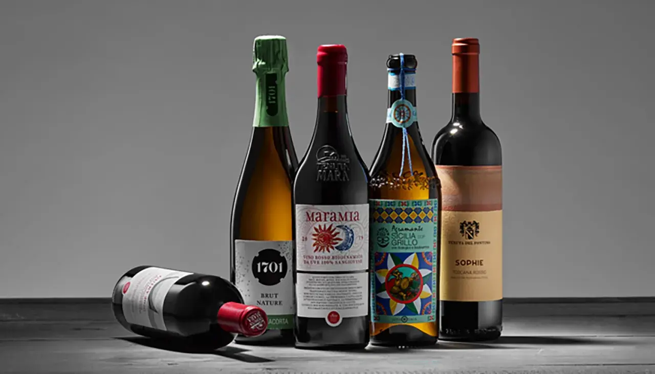 Fünf Flaschen Wein, darunter ein Sekt und vier Rotweine, stehen auf einem Tisch. Einer der Rotweine liegt vorn. Ein Etikett weist auf biodynamischen Wein hin.