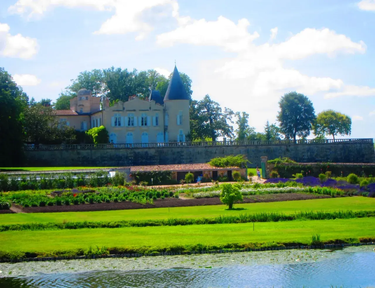 Schloss mit Türmchen und Gartenanlage, davor ein Teich.