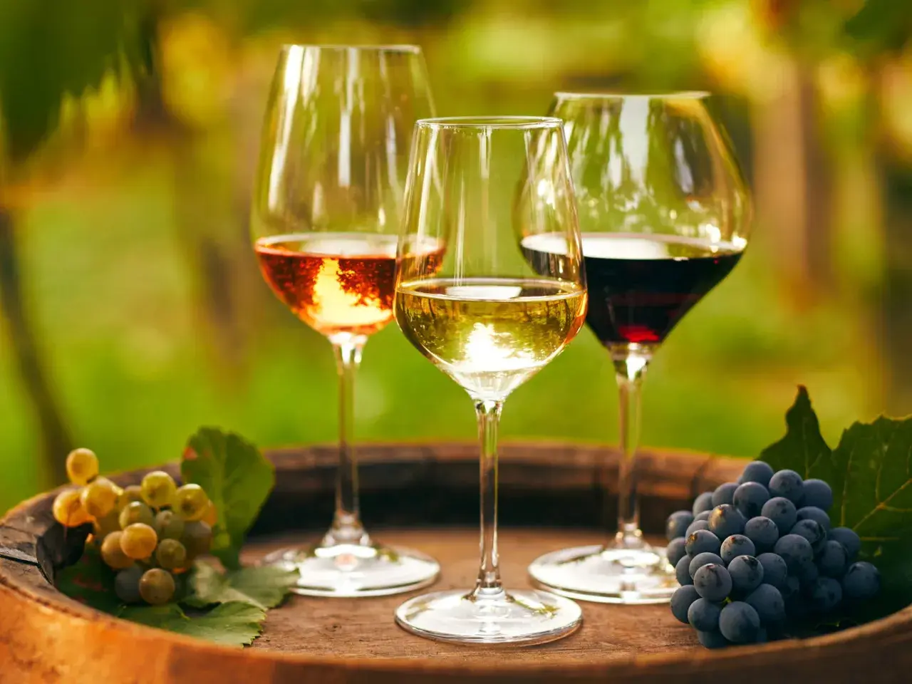 Drei Gläser Wein – Rosé, Weiß und Rot – stehen auf einem Holzfass. Daneben Trauben, die an einen Besuch im **Château Lafleur** erinnern.