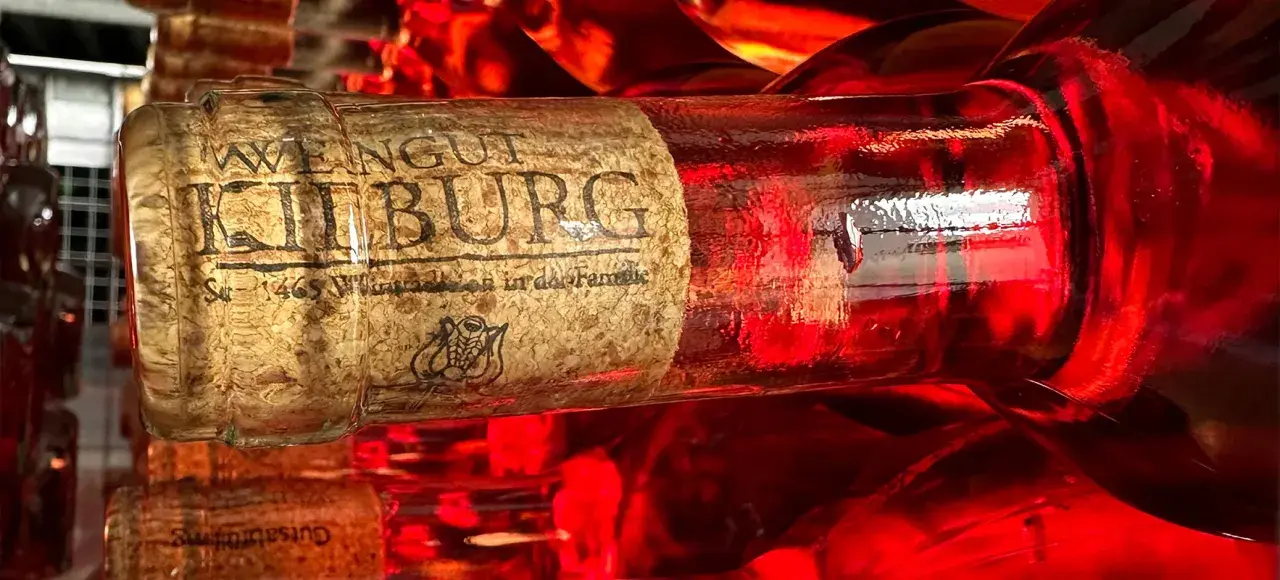 Rotwein-Flasche mit dem Etikett "Weingut Kilburg" im Vordergrund. Ein typischer Mosel Wein, der in der Sonne glänzt.