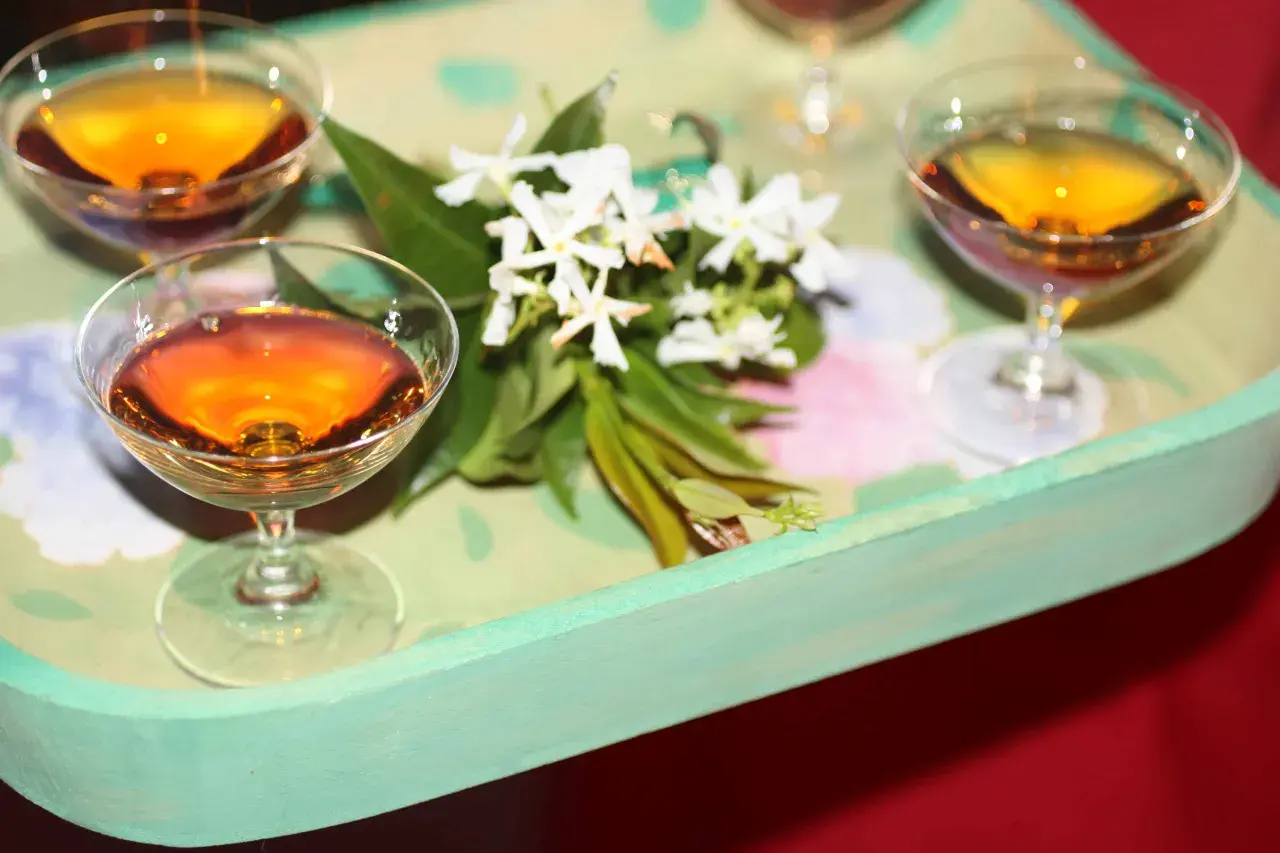 Bernsteinfarbene Likörgläser auf einem Tablett mit Blumen. Eine elegante Alternative zu Vin Santo für besondere Anlässe.