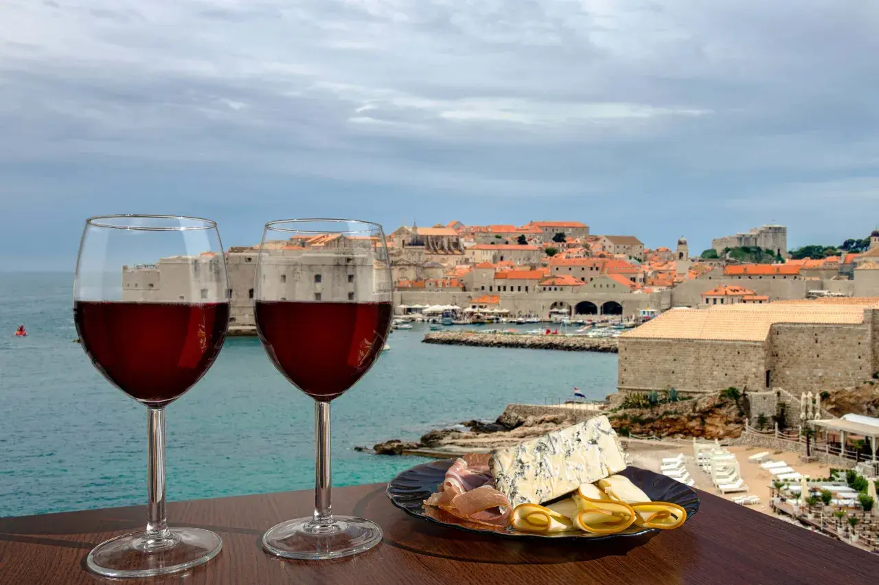 Zwei Gläser Rotwein und eine Käseplatte mit Schinken vor der Kulisse von Dubrovnik. Eine perfekte Weinprobe in Kroatien.