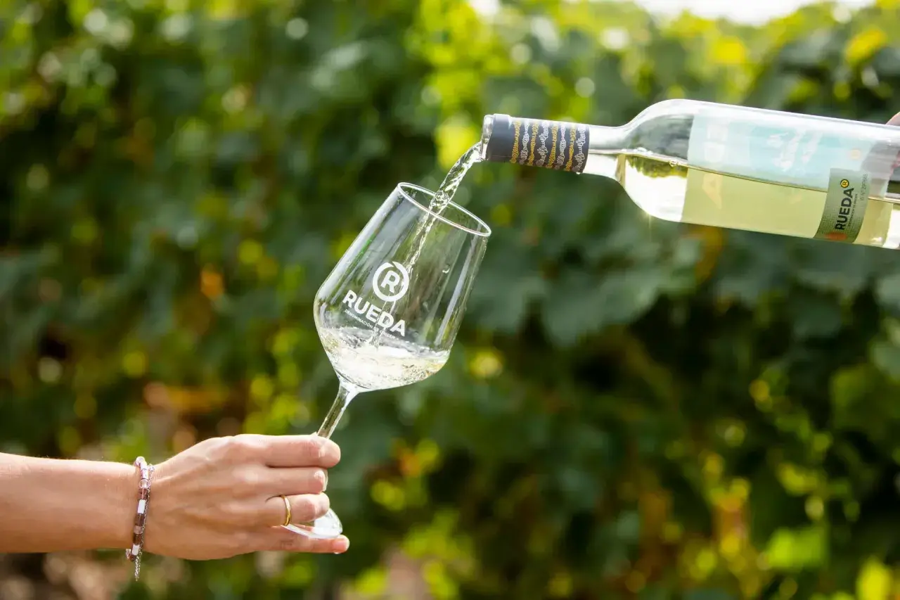 Ein Glas wird mit Weißwein gefüllt, der aus einer Flasche mit dem Etikett "Rueda" gegossen wird. Ein Hauch von verdejo deutsch in der Luft.