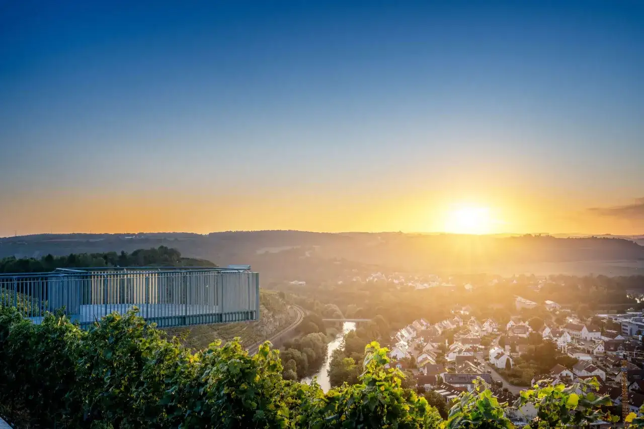 Sonnenuntergang über Weinbergen und einem Dorf bei Stuttgart. Eine Aussichtsplattform bietet Blick auf die Landschaft.