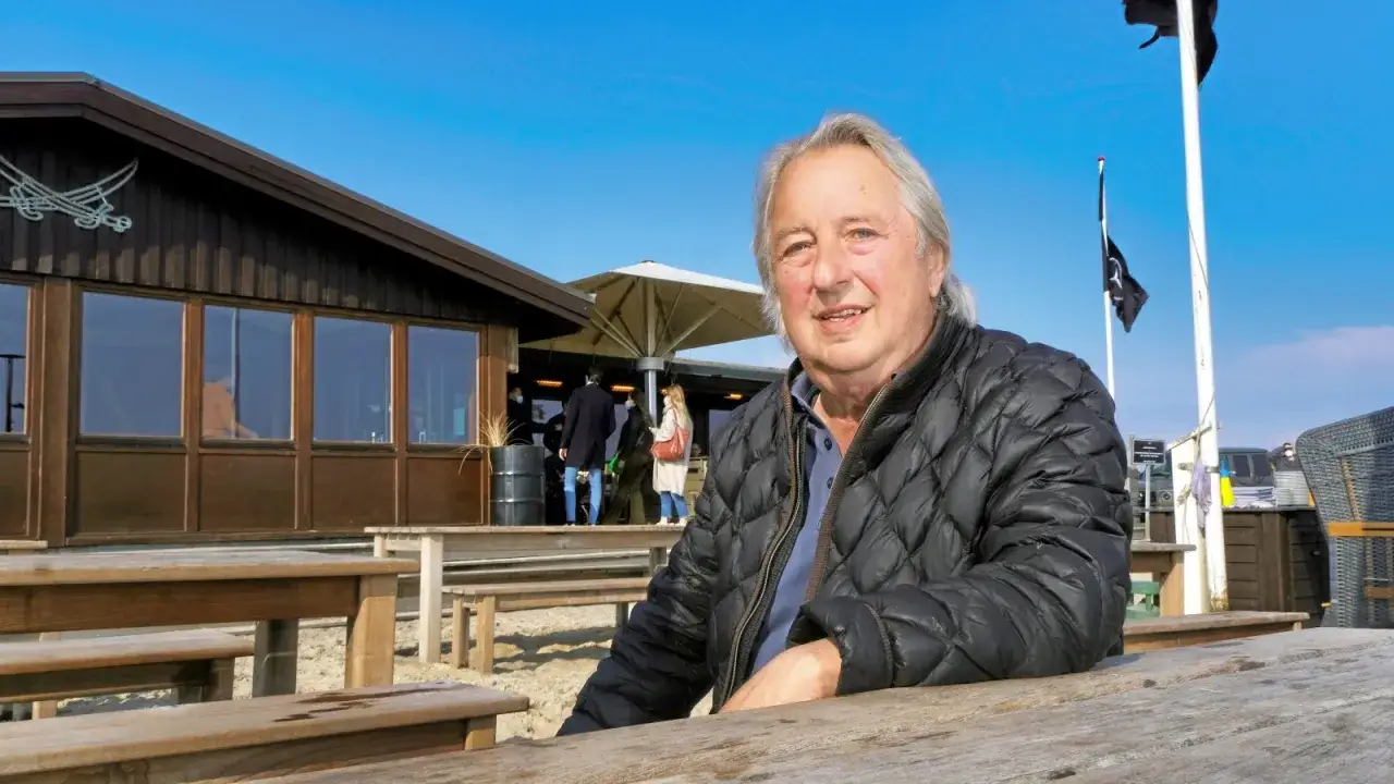 Herbert Seckler sitzt an einem Holztisch vor einem Strandrestaurant.