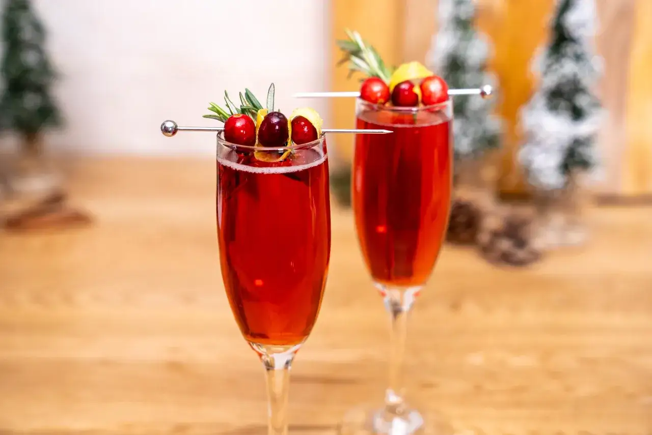 Zwei festliche Gl&auml;ser mit rotem Champagner-Drink, garniert mit Cranberries, Rosmarin und Zitronenzeste.