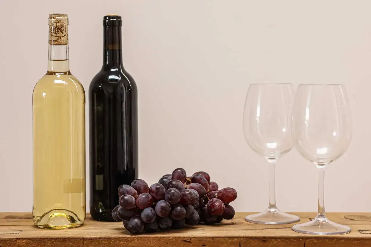 Zwei Flaschen Wein, eine helle und eine dunkle, mit einer Traube und zwei Gl&auml;sern. Perfekt f&uuml;r die bester rotwein rangliste.