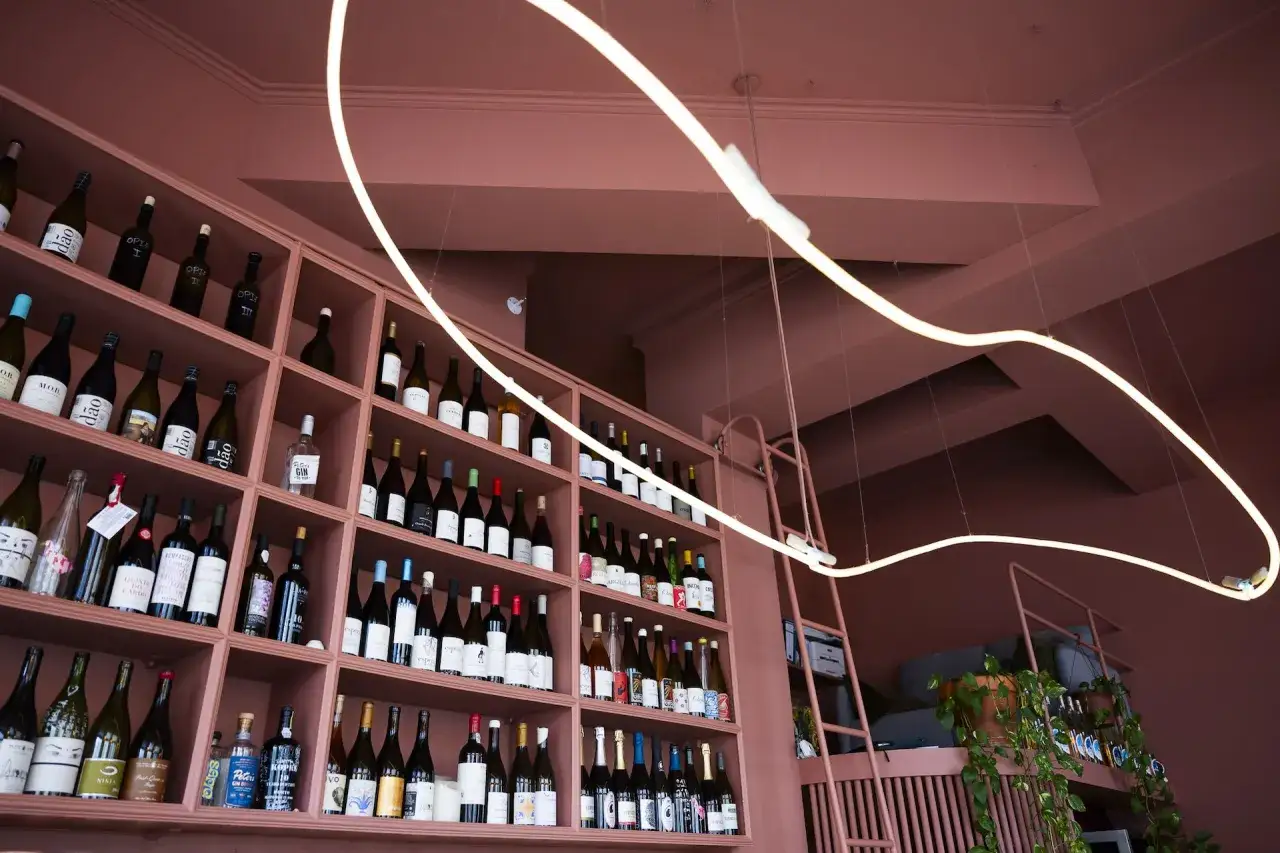 Regale voller Flaschen in einer glasweise Weinbar. Ein geschwungenes Lichtband beleuchtet die Auswahl.