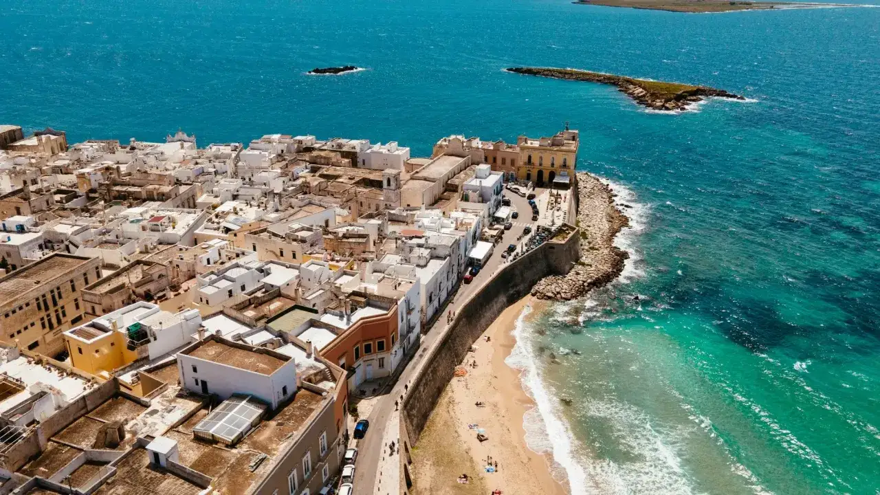 Wei&szlig; get&uuml;nchte H&auml;user dr&auml;ngen sich an der K&uuml;ste von Salento, Italien, mit t&uuml;rkisfarbenem Wasser und einem Sandstrand.