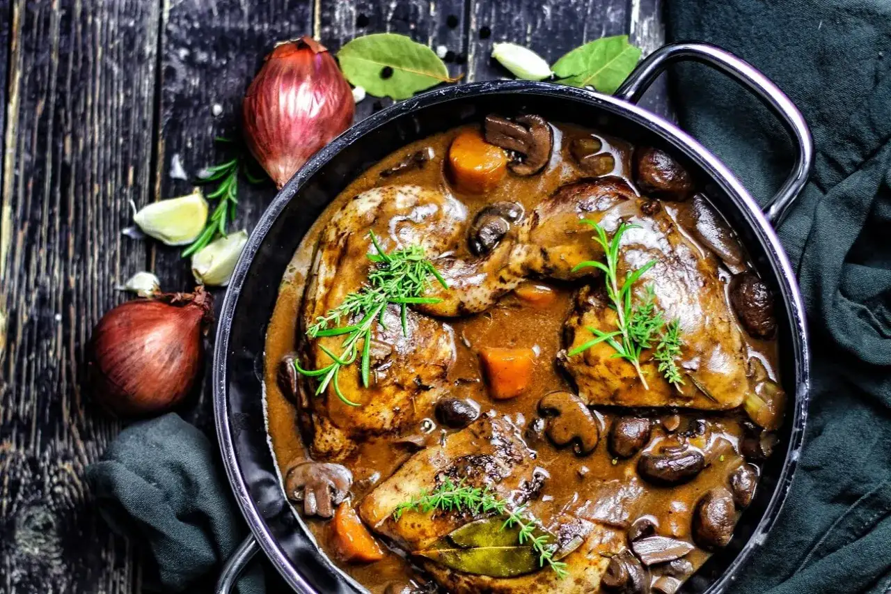 Ein k&ouml;stliches Coq au Vin, ein ganzes Huhn in einer reichhaltigen Rotweinso&szlig;e mit Pilzen und Karotten, garniert mit Rosmarin.