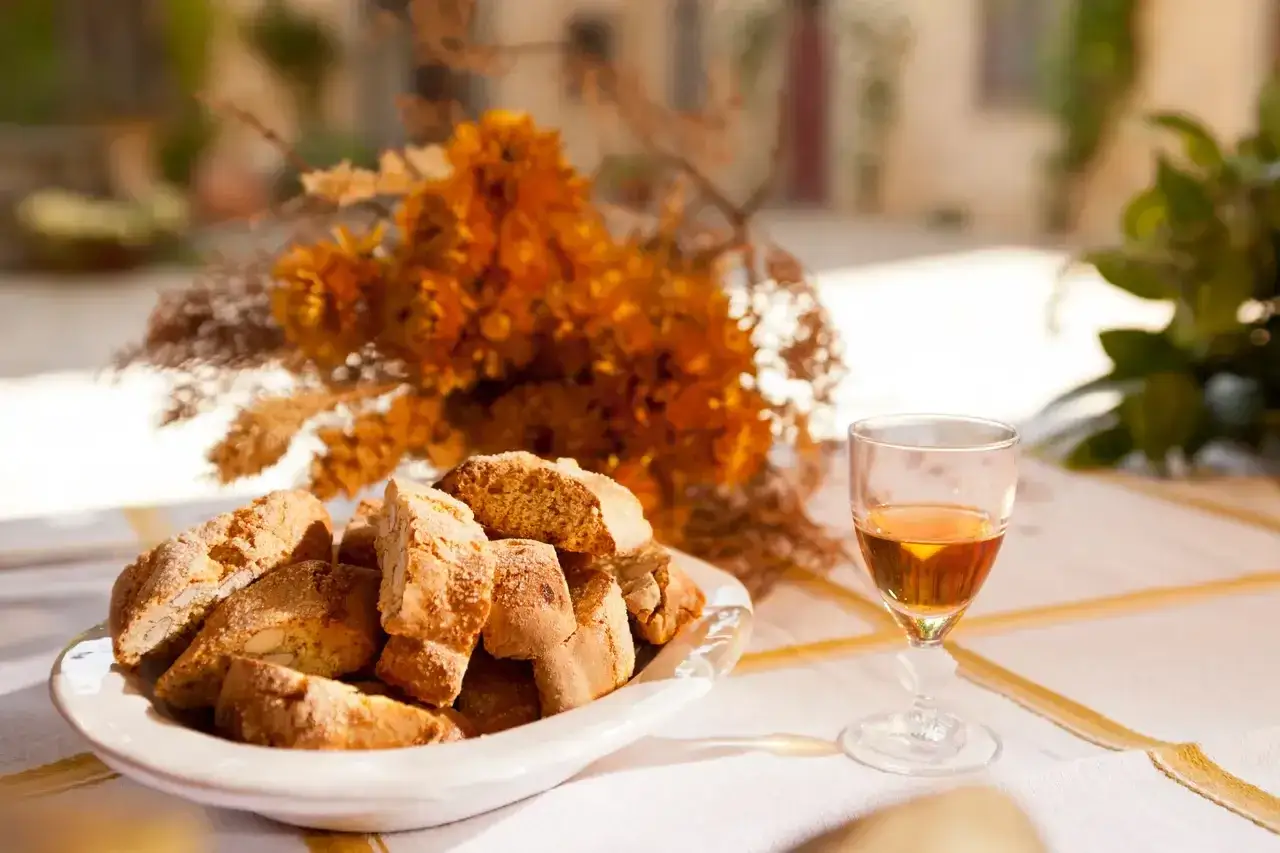Biscotti und ein Glas süßer Dessertwein aus der Toskana auf einem Tisch mit Herbstblumen.