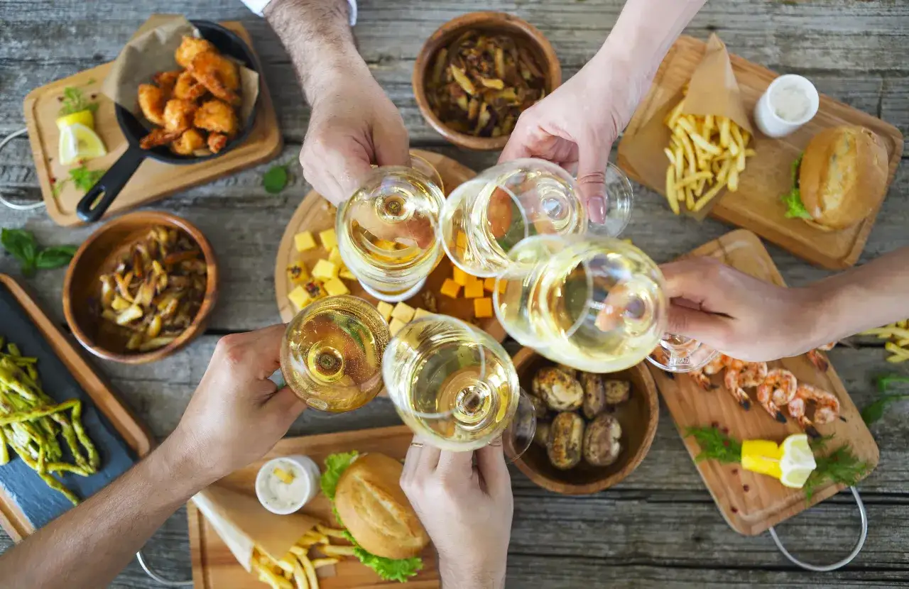Hände stoßen mit Weißwein an. Der frische sauvignon blanc geschmack passt perfekt zu Garnelen, Pommes und kleinen Burgern.